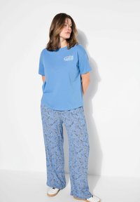 Camiseta de algodón azul claro con un diseño impreso, combinada con pantalones holgados de azul con un patrón paisley y zapatillas blancas.