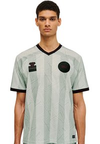 Ljusgrön fotbollströja med geometriskt mönster, svarta detaljer och V-hals. Har logotyper på vänster bröst och ärm.