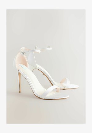 Baltie augstpapēžu sandales, kas izgatavotas no gludas satīna materiāla, ar atvērtu purngali, slaidiem potīšu siksniņām un stila augsto papēdi.