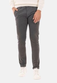 Pantaloni di cotone grigi con un design slim fit, dotati di tasche laterali, chiusura a bottone e cuciture rinforzate alle ginocchia. Indossati con sneakers bianche.