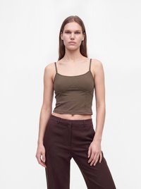 Jeune femme aux longs cheveux raides portant un top court marron et un pantalon taille haute marron foncé sur fond blanc.