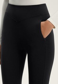 Leggings neri a vita alta con un design elegante, dotati di una tasca con zip e di un tessuto liscio e elastico per comfort e libertà di movimento.