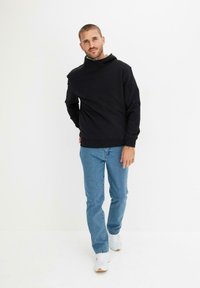 Felpa nera con collo alto, abbinata a jeans azzurri chiari e sneakers bianche. Il tessuto sembra morbido e dallo stile casual.