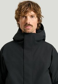 Svart vattentät jacka med hög krage och dold dragkedja. Har en enkel design och slät textur, lämplig för aktiv användning.