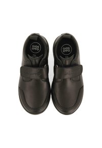 Zapatos de cuero negro con una correa de velcro y suela de goma texturizada. Diseño redondeado con logotipo en la correa, superficie lisa y estilo minimalista.