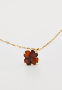 Zlata verižica z obeskom v obliki štiriperesne deteljice, ki je izdelana iz rjave smole, z sijočimi zlatimi poudarki na konicah vsakega lista.