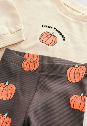 Felpa crema con testo "Little Pumpkin" e grafica di una zucca arancione, abbinata a leggings a coste grigio scuro con motivi di zucche ripetuti.