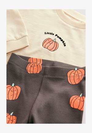 Tejfehér pulóver "Kis tök" felirattal és narancssárga tök grafikával, sötétszürke bordázott leggings-szel párosítva, amely ismétlődő tök mintákkal rendelkezik.