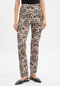 Beige broek met leopardenprint, voorzien van donkerbruine en zwarte vlekken. Strak ontwerp met een gladde textuur. Gemonteerd met zwarte platte schoenen.