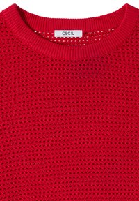 Pull en maille rouge avec col rond et texture gaufrée, avec une étiquette blanche portant le nom de la marque « CECIL » à l'intérieur de l'encolure.