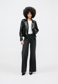 Mustast nahast mootorratturi jakk lukuga taskutega, valge T-särk ja kõrge vöökohaga mustad laiade säärtega teksad. Model kannab musti kõrge kontsaga kingi.