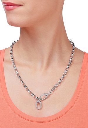 Collier en chaîne argentée avec de grandes mailles ovales, porté autour du cou sur un haut corail à encolure dégagée.