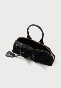 Juodas krokodilo odos raštas rankinys su auksine užtrauktuku, dviem rankenomis ir mažyte prisegama etikete ant balto fono.