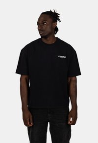 Černé bavlněné tričko s krátkými rukávy, kulatým výstřihem a bočními švy. Na levé straně se nachází bílý text "Crystal Paris".