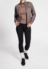 Gray zip-up jacket with black stripes, brown fitted top, and black leggings. Features logo accents and black athletic shoes with white socks.