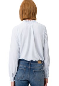 Himmelbluse mit gestreiften Muster, Rüschenausschnitt, langen Ärmeln und Knopfmanschetten, kombiniert mit dunkelblauen Jeans in mittlerer Waschung.