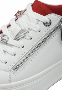 Sneaker in pelle bianca con accento rosso, dotato di dettagli metallici a forma di stella e fulmine, lacci bianchi e una cerniera laterale.