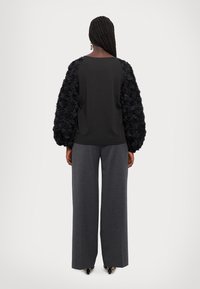 Haut noir avec des manches florales texturées, associé à un pantalon large gris. Le haut présente un design simple avec un col rond.