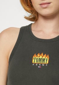 Débardeur côtelé gris avec l'inscription "TOMMY JEANS" brodée en flammes colorées, doté d'un col en U et d'une coupe ajustée.
