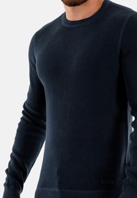 Maglione blu navy realizzato in tessuto testurizzato, con scollo rotondo e maniche lunghe. Include una piccola etichetta con il marchio nella parte inferiore.