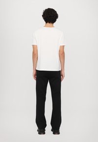 Weißes Baumwoll-T-Shirt mit Rundhalsausschnitt und kurzen Ärmeln, kombiniert mit schwarzen Hosen, die ein einfaches und entspanntes Design von hinten zeigen.