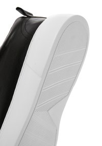 Scarpa in pelle nera con suola in gomma bianca. Presenta una superficie testurizzata per la presa sulla suola e un tab per il tallone per facilitarne l'indossamento.