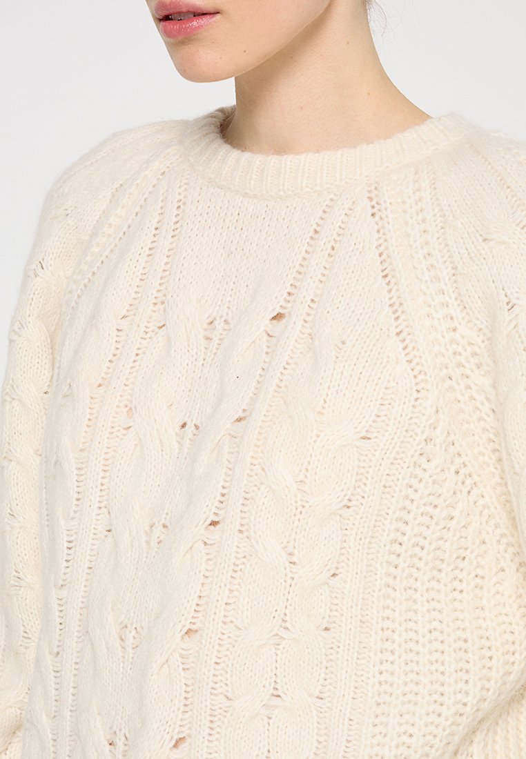 Dicker gestrickter Pullover in Creme mit Kabelmuster, geripptem Rundhalsausschnitt und weicher Textur. Hergestellt aus kuscheligem Garn für Wärme.