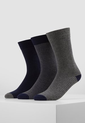 Trois paires de chaussettes pour hommes dans des couleurs sombres : bleu marine uni, gris foncé avec un motif chevrons, et gris clair à rayures. Bords côtelés et orteils contrastés.