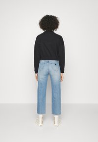 Sudadera negra recortada de manga larga combinada con vaqueros de pierna ancha en azul claro. Los vaqueros presentan un detalle triangular en el bolsillo trasero y un lavado desgastado.