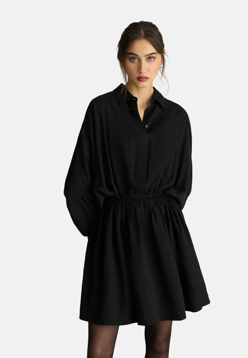 Czarna sukienka koszulowa z kołnierzykiem, długimi rękawami, elastyczną talią i rozkloszowanym dołem. Wykonana z lekkiej tkaniny o gładkiej fakturze.