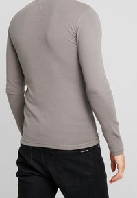 Graues Langarmshirt aus weichem Stoff, mit körpernahem Schnitt, rundem Ausschnitt und sichtbaren Nähdetails.