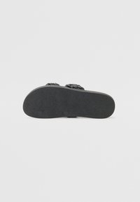 Sorte sandaler med teksturert såle. Vevd stroppedesign over toppen. Flat form, minimal maskinvare, egnet for uformell bruk.