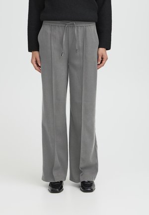 Pantaloni larghi grigi in morbido tessuto con vita regolabile e dettagli plissettati sul davanti. Scarpe nere completano l'outfit.