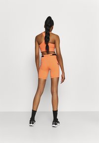 Conjunto deportivo naranja de top corto y shorts hechos de tejido elástico. Presenta un diseño de espalda de nadador, forma ajustada y detalles en negro contrastante.