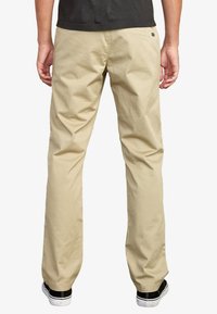 Beige cotton chinos with a relaxed fit, featuring five pockets, flat front, and a smooth texture, paired with black sneakers.