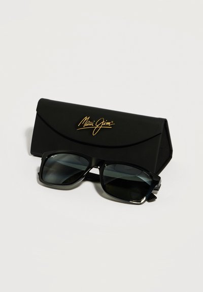 Μαύρα ορθογώνια γυαλιά ηλίου με σκούρους φακούς που ακουμπούν μπροστά σε μια μαύρη διπλωτή θήκη με χρυσή επωνυμία «Maui Jim».