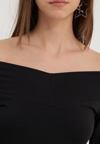 Haut noir décolleté avec un design ajusté, présentant un col en V et une texture lisse. Grandes boucles d'oreilles en forme d'étoile visibles.