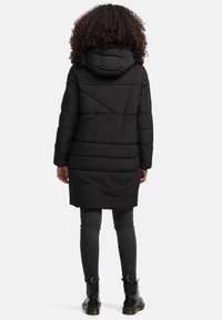 Zwarte pufferjas met capuchon, gequilt ontwerp, lange mouwen en een lengte tot midden boven de dij. Draag over donkergrijze leggings en zwarte laarzen.