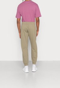 Ljust lila bomullströja i kombination med beige sweatpants. Byxorna har resår i midjan och vid anklarna. Modellen bär vita sneakers.