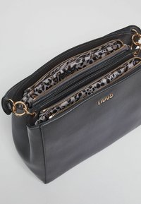Sac à main en cuir noir avec quincaillerie dorée et plusieurs compartiments zippés. L'intérieur présente un doublage en motif léopard gris et noir.