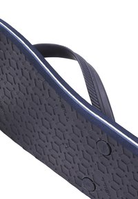Meripantofli navy yang menampilkan sol karet bertekstur dengan pola sarang lebah, dan disorot oleh garis putih di sepanjang tepi.