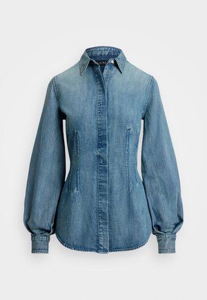 Lyseblå denimskjorte med spiss krage, puffermer og sidelommer. Har knappelukking og en buet nederkant.
