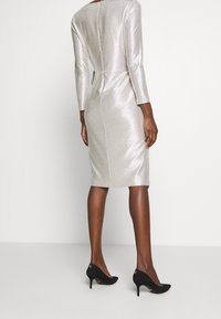 Silver, knälång klänning med långa ärmar och en smal silhuett, som har en subtil glittrande textur. Kombinerad med svarta klackskor.