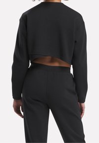 Černá zkrácená mikina s dlouhými rukávy, hladkou texturou, kulatým výstřihem a otevřeným designem na zádech. Spárováno s odpovídajícími černými kalhotami.
