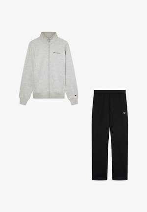 Sudadera gris con cremallera y cuello alto, con un pequeño logo en el pecho, combinada con pantalones de chándal negros que tienen bolsillos laterales y un logo en la cadera.