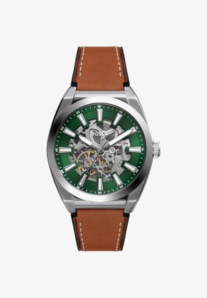 Montre-bracelet Fossil en acier inoxydable avec cadran squelette vert, index blancs, aiguilles argentées, rouages visibles et bracelet en cuir marron avec surpiqûres.
