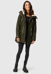 Olijfgroene parka jas met een zachte bontvoering in de capuchon, trekkoorden en leren accenten. Gepaard met zwarte skinny jeans en dikke zwarte laarzen.