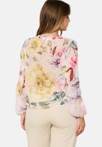 Blusa floreale con maniche lunghe e a sbuffo. Tessuto trasparente e leggero con grandi fiori rosa e gialli vivaci, e una finitura morbida e текстurizzata.