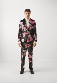Black suit covered in large pink and white rose patterns, with a white shirt underneath and black shoes. Tailored fit with a modern design.