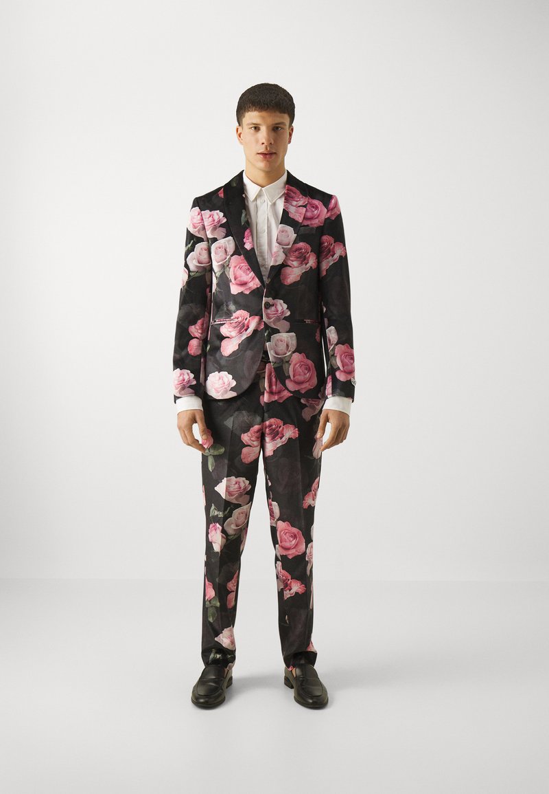 Black suit covered in large pink and white rose patterns, with a white shirt underneath and black shoes. Tailored fit with a modern design.